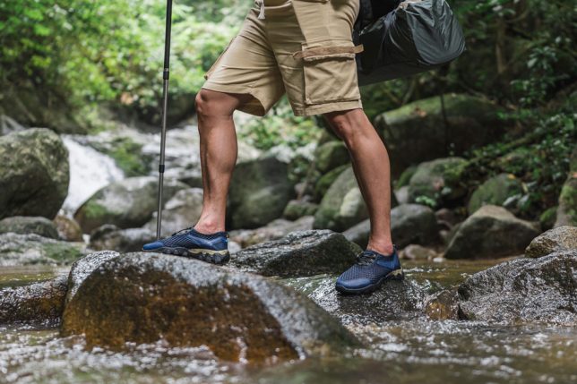 A photo of a hiker holding hiking poles about to walk across rocks to cross a river.
